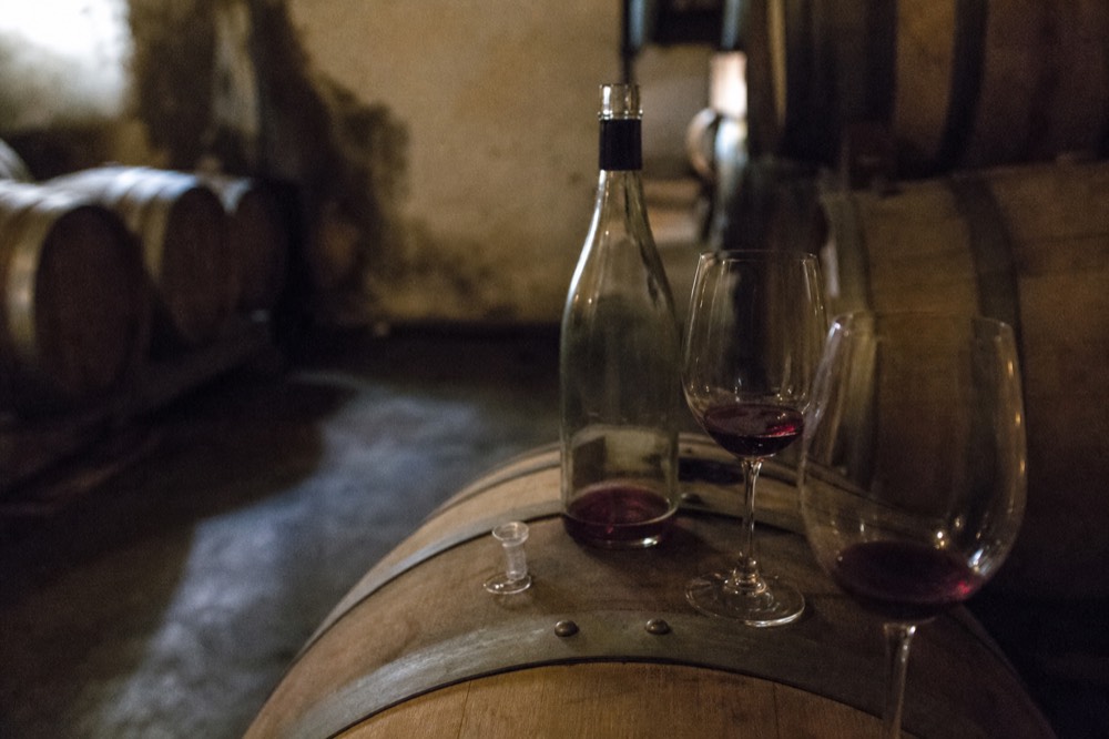 An open bottle and glasses on a barrel in a dim cellar, no text, no logos, no people