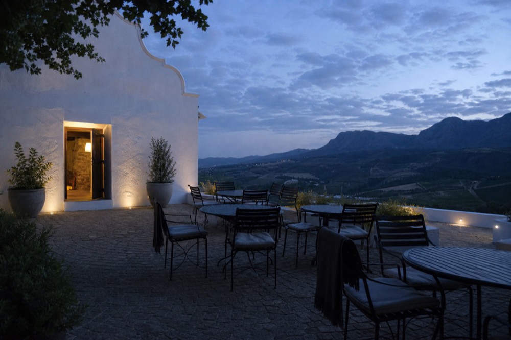 Quiet vineyard terrace with empty tables and chairs overlooking valley slopes, no text, no logos, no people