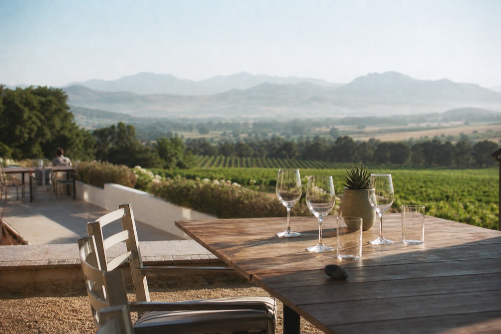 A cellar door terrace with empty tasting glasses and vineyard views, no text, no logos, no people