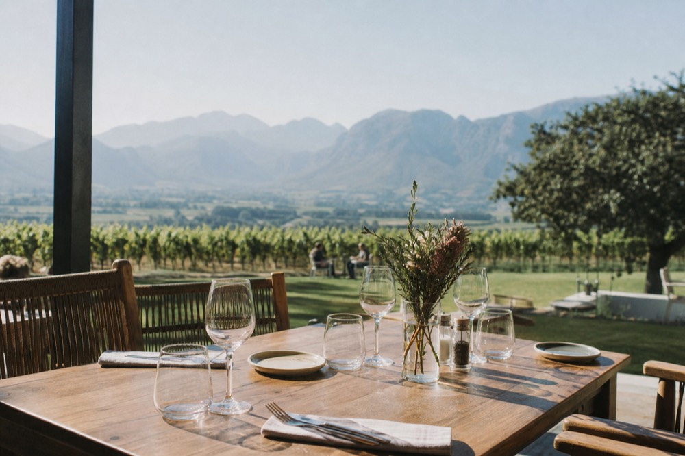 Table set for lunch on a wine estate terrace overlooking vines, no text, no logos, no people