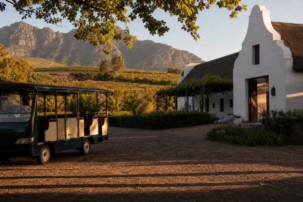 Open-air tram-bus parked at a Franschhoek wine estate with vineyards behind, no text, no logos, no people